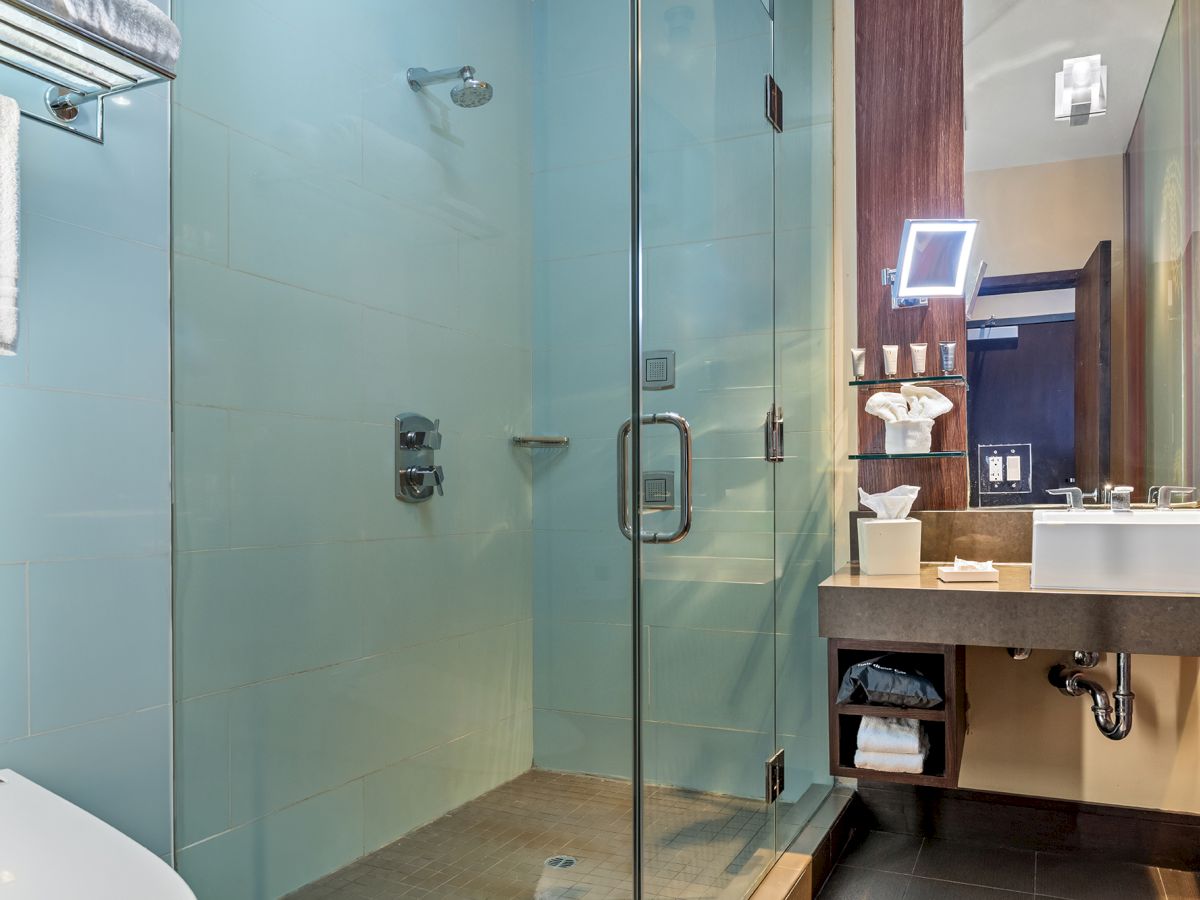 The image shows a modern bathroom with a glass-enclosed shower, sink with mirror, and neatly organized towels and toiletries.