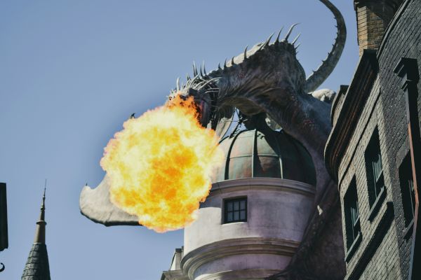 A dragon on top of a building breathing fire, set against a clear sky, with architectural details visible on the building.