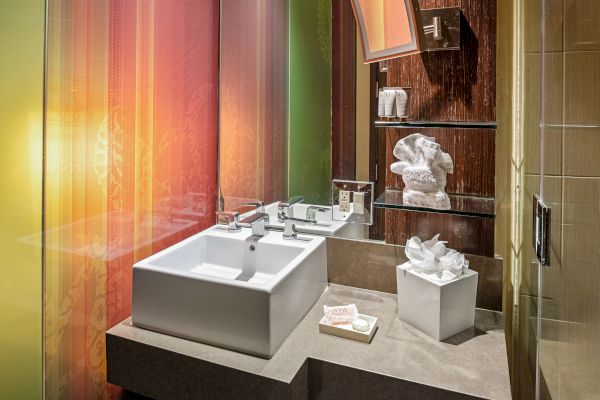 A modern bathroom with a square sink, colorful walls, toiletries, and towels arranged on shelves and a countertop.