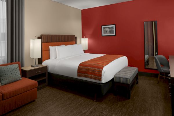 The image shows a hotel room with a large bed, bedside tables, a sofa, and a desk. The walls are red and beige.