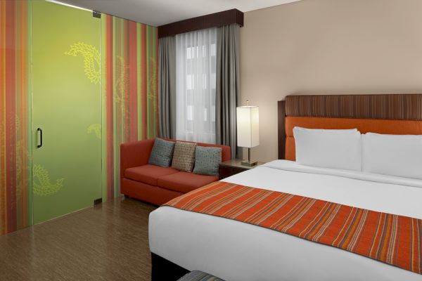 A hotel room with a bed, orange-striped bedding, a sofa, a lamp, and a decorative green sliding door.