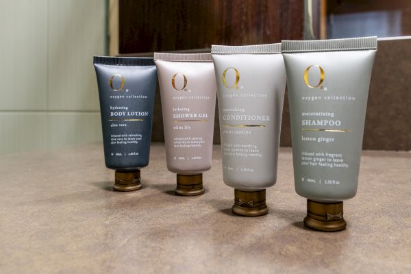 The image shows four tubes: body lotion, shower gel, conditioner, and shampoo, displayed on a countertop.