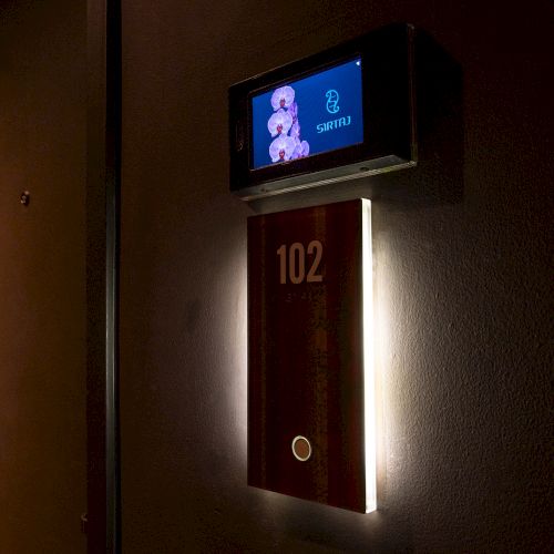 A door sign with the number 102, softly illuminated, beneath a display showing an animated character and the word 