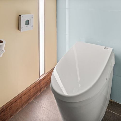 A modern bathroom with a sleek white toilet, toilet paper holder, and wall-mounted control panel on a light-colored wall.