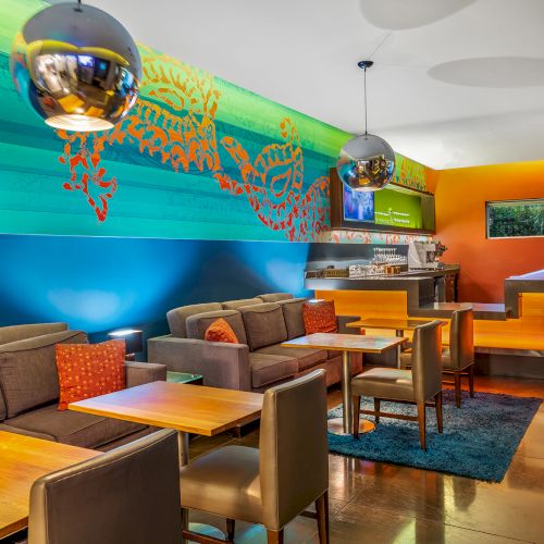 A modern lounge with colorful decor, featuring cozy seating, bright wall art, tables, and ambient lighting.