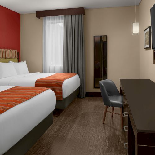 The image shows a hotel room with two beds, a TV, desk, chair, and curtain. The decor is modern with warm colors and hardwood flooring.