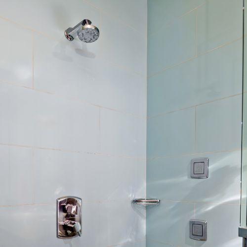 A shower space with a modern showerhead, a faucet, and a glass door, featuring white-tiled walls.